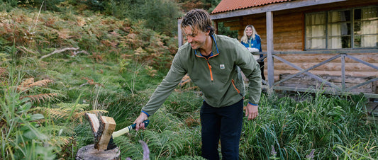 A man cutting logs by a cabin